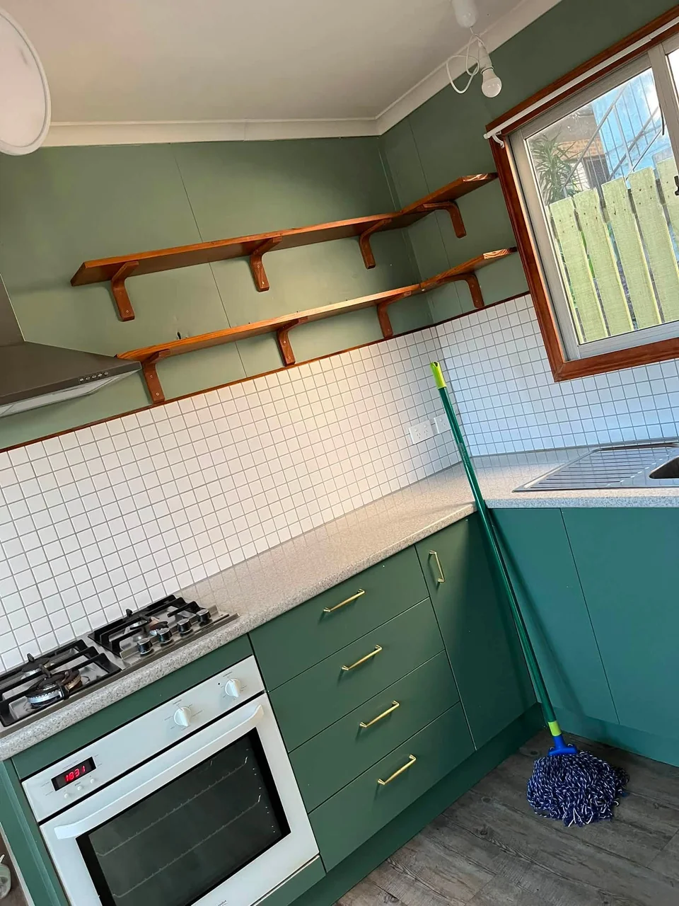 Green kitchen cabinets, timber shelves and a mop during an S-Con clean