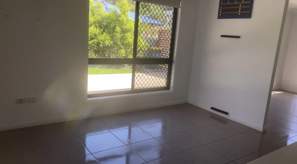 Empty room with grey floor tiles, white walls and a large screened window.